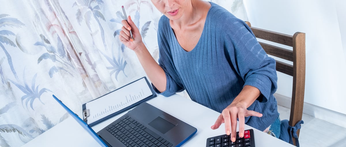 mujer irreconocible usando calculadora hace cuentas de la empresa calculando beneficios y perdidas del estocaje anual. Mujer de negocios sentanda en el escritorio analiza los numeros usando el ordenador