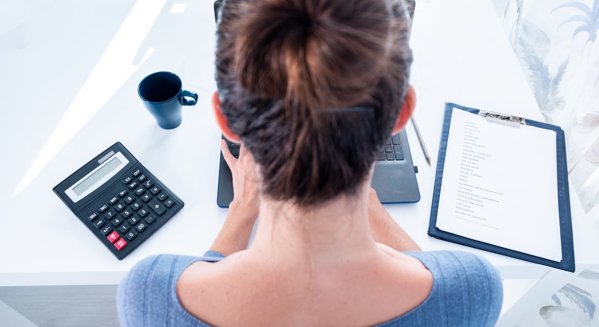 mujer de espaldas esta haciendo cuentas y calculando gastos para llegar a final de mes. Señorita usando la calculadora y el ordenador portatil con una montaña de papeles que entregar a su jefe. Concepto de trabajo duro de oficina. Mujer emprendedora calcu